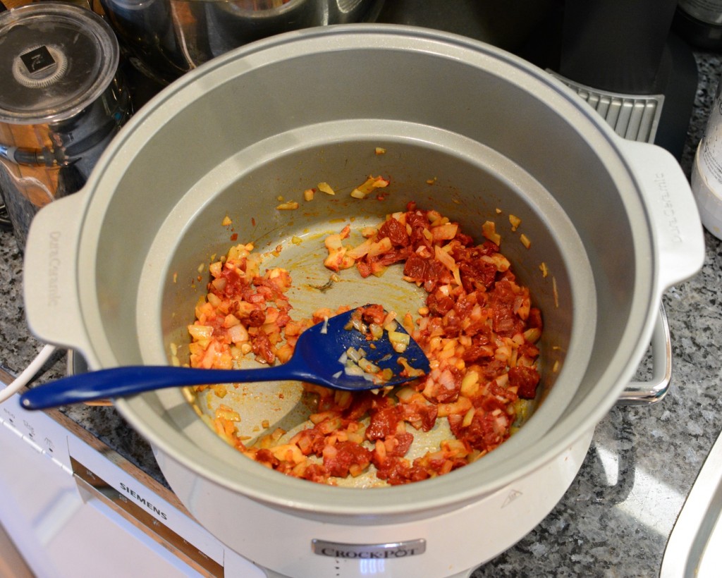 Fräs lök, vitlök och tomatpuré i grytan på spisen.