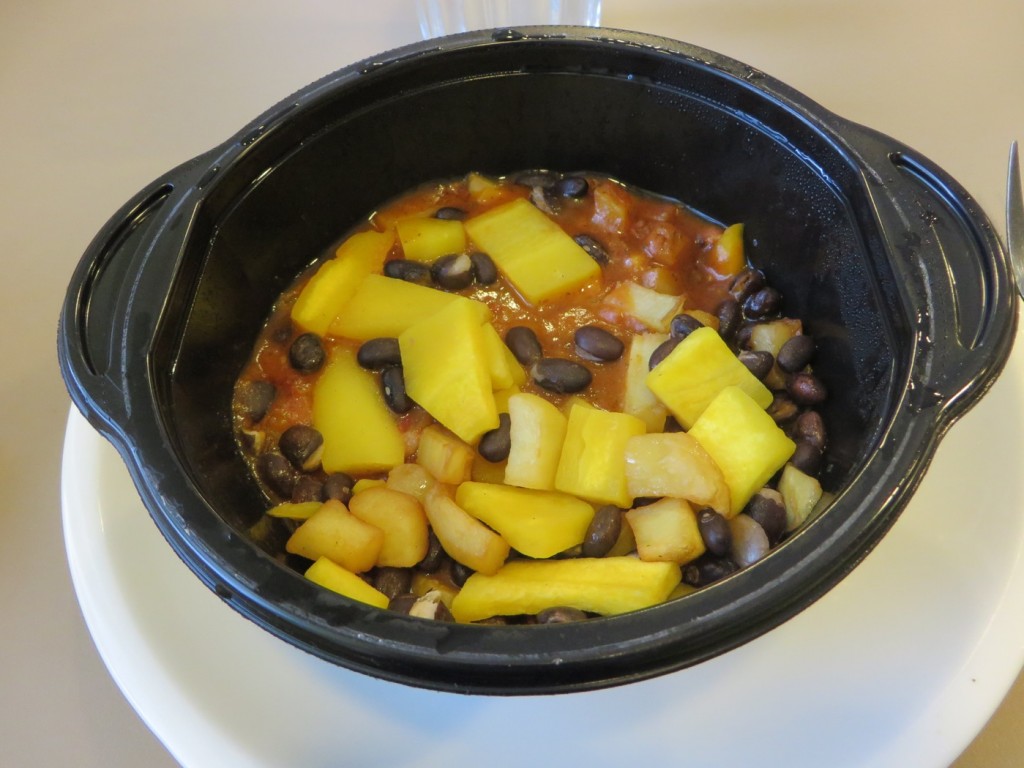 Stekt potatis som täcks av en långkokt vegansk gryta och toppad med svarta kidneybönor och gul morot